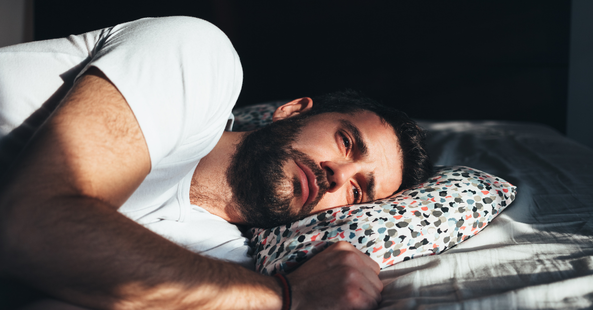 A man suffering from seasonal depression laying in his bed looking forlorn