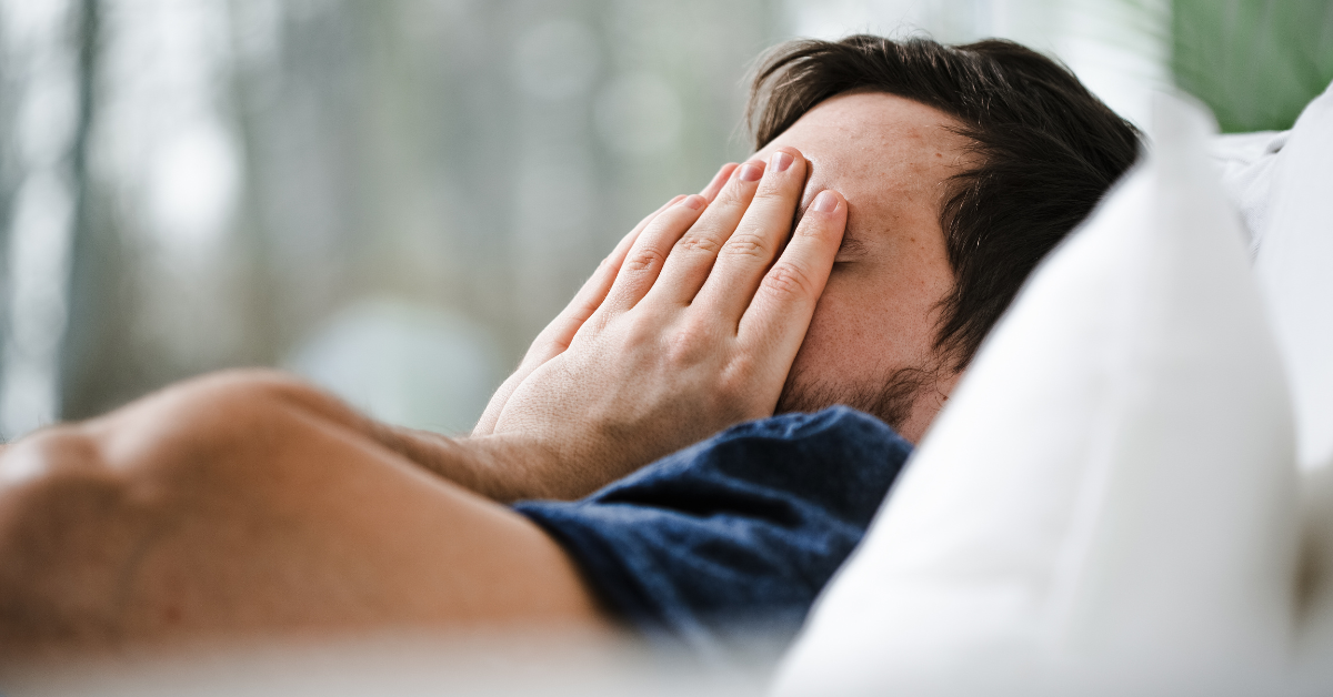 A man laying in beds with his hands on his face suffering from alcohol withdrawal