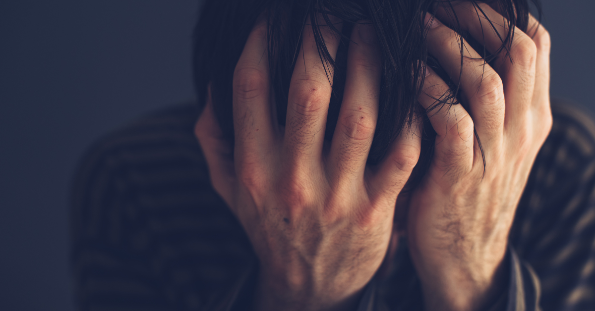 A man with small cuts on his hands, hiding his face in his hands experiencing common drug withdrawal symptoms