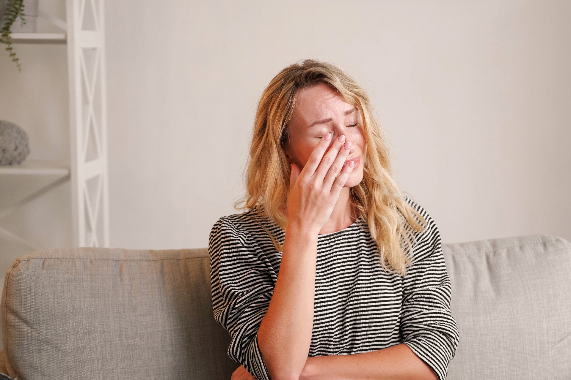 A woman sitting on her couch while crying, struggling with a cyclothymic disorder or Cyclothymia.