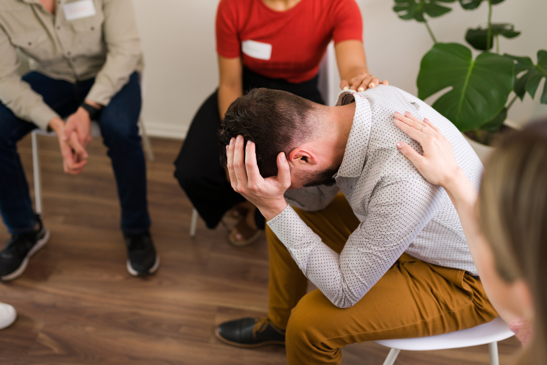 A man in group therapy with his head in his hands being supported by others while he discusses his opioid addiction