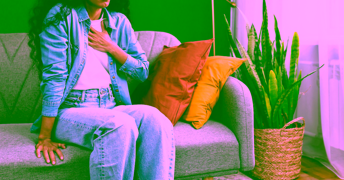 A woman on a couch with her hand on her chest having a panic attack