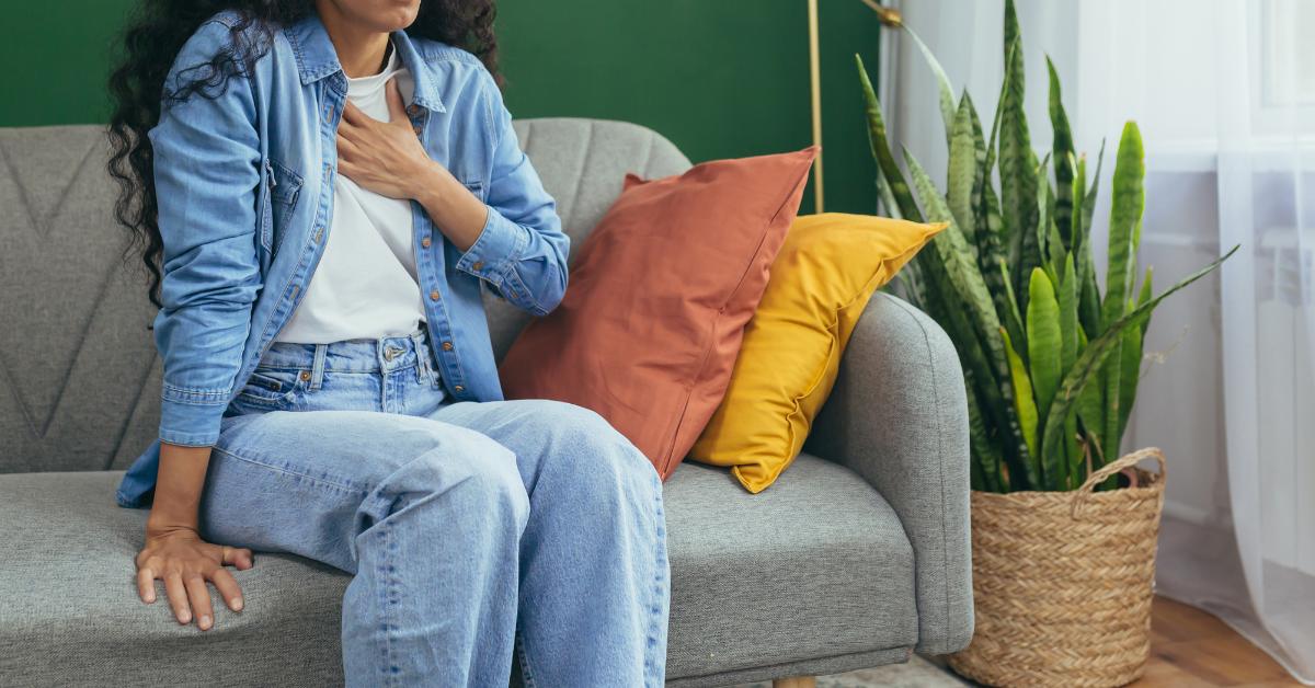A woman on a couch with her hand on her chest having a panic attack
